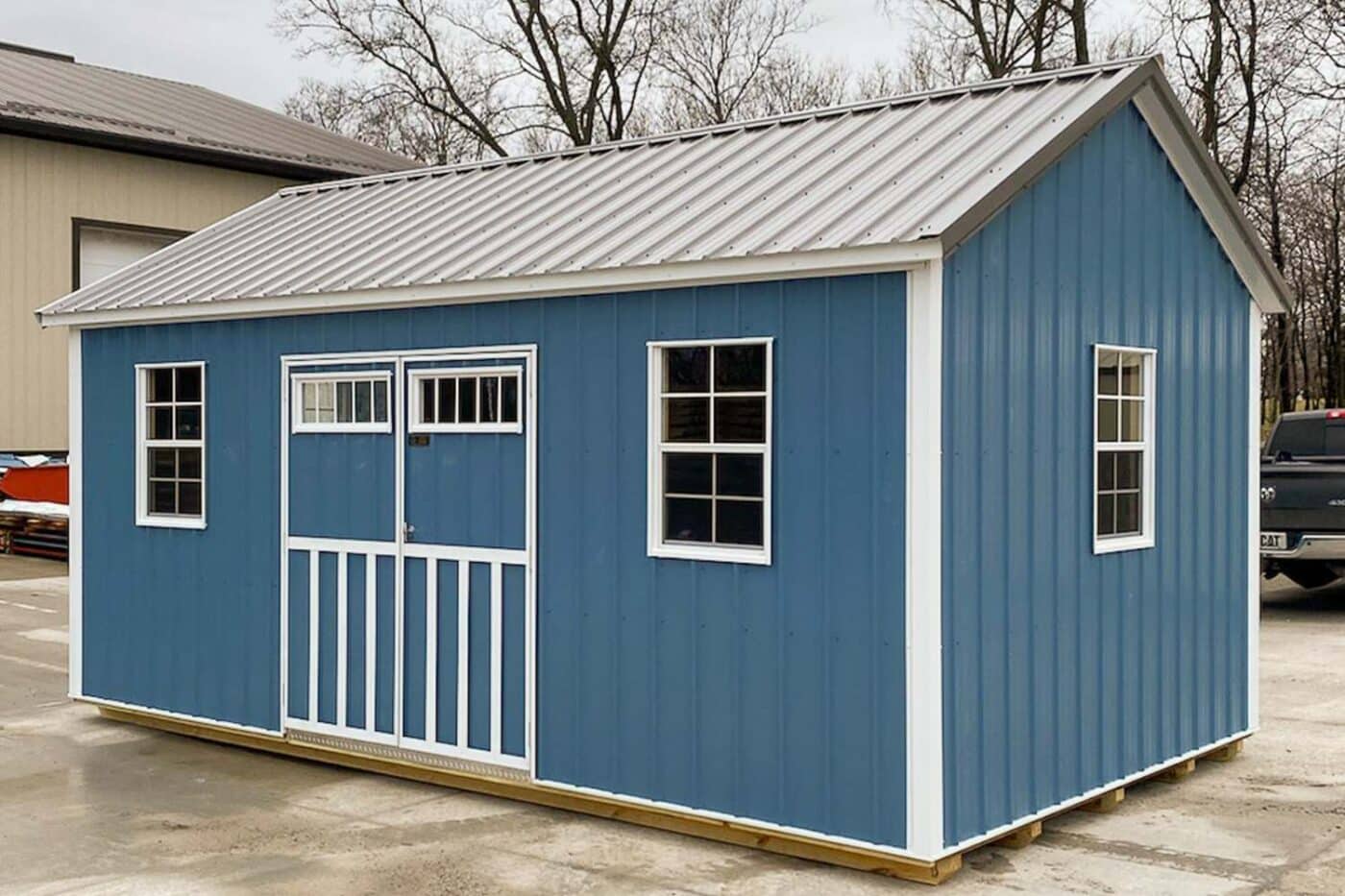 Blue and white metal shed with gray metal roof, double doors, and three windows